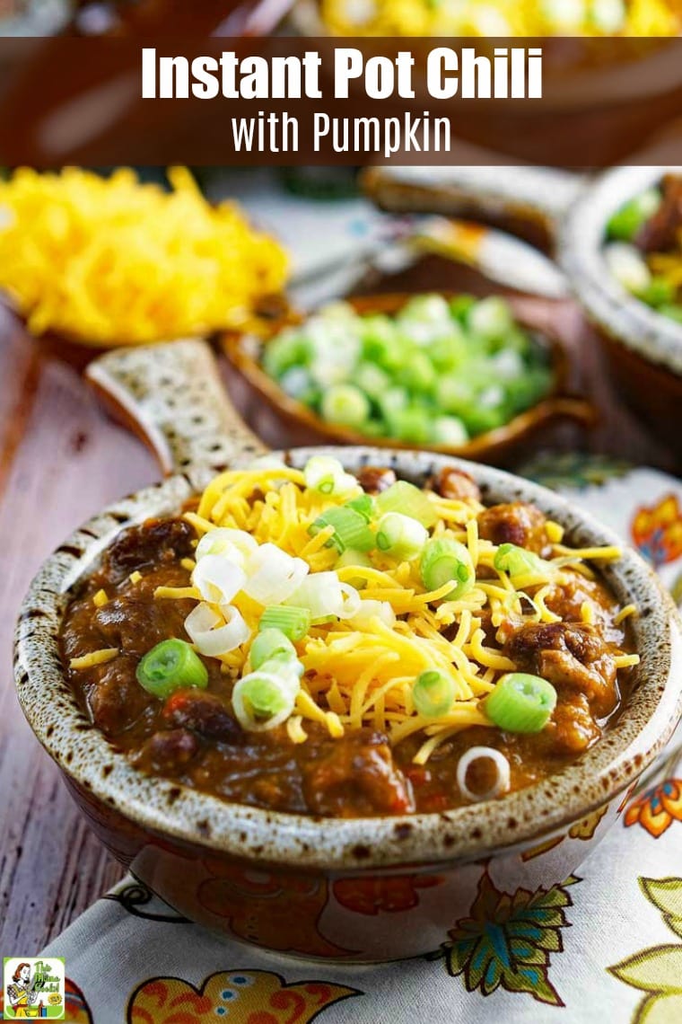 Close up of Instant Pot Chili with Pumpkin with shredded cheese and chopped green onions served in a lug handled bowl. 