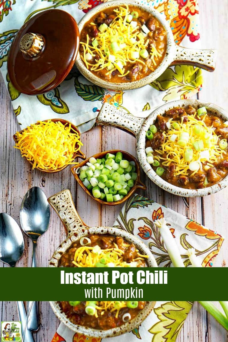 Overhead of lug handled bowls of Instant Pot Chili with Pumpkin with shredded cheese and chopped green onions with bowls of shredded cheese, floral napkins, and spoons.