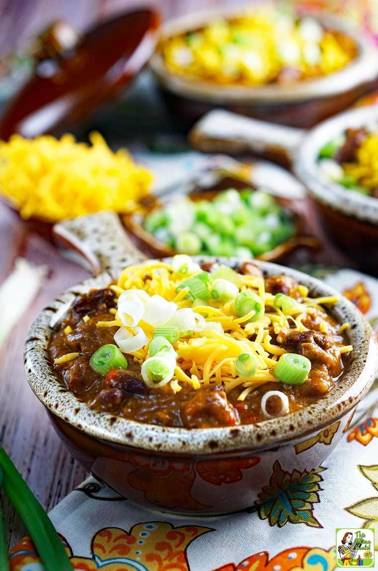 Close up of a bowl of pumpkin chili with shredded cheese and chopped green onions.