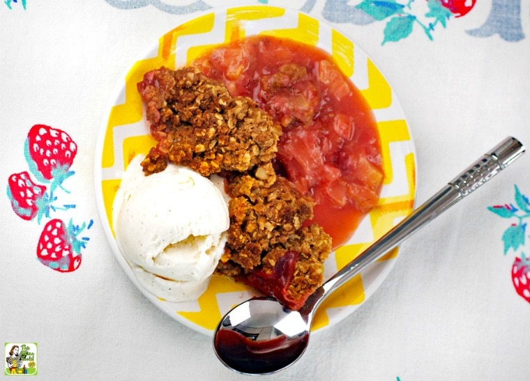 A plate of strawberry rhubarb crisp with a scoop of vanilla ice cream and a spoon.