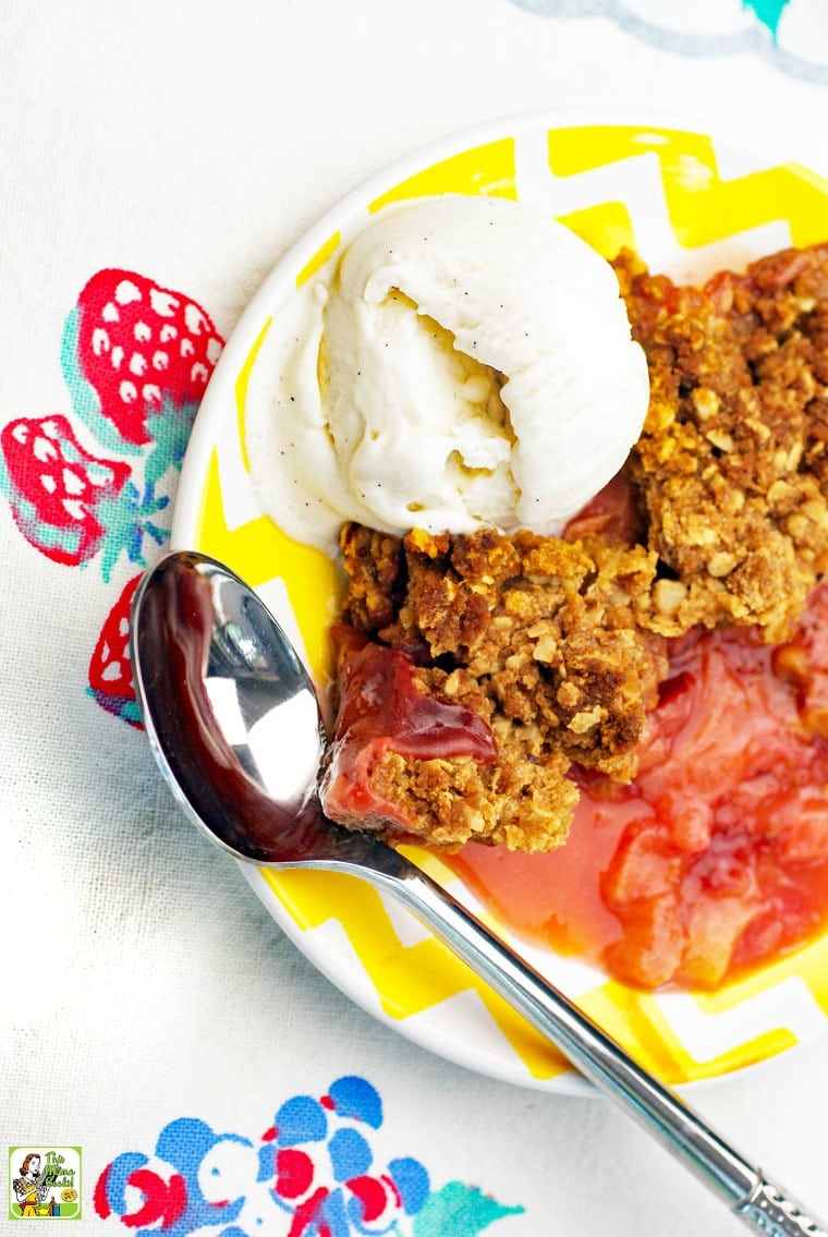 A yellow plate with rhubarb crisp and a scoop of vanilla ice cream and a spoon.