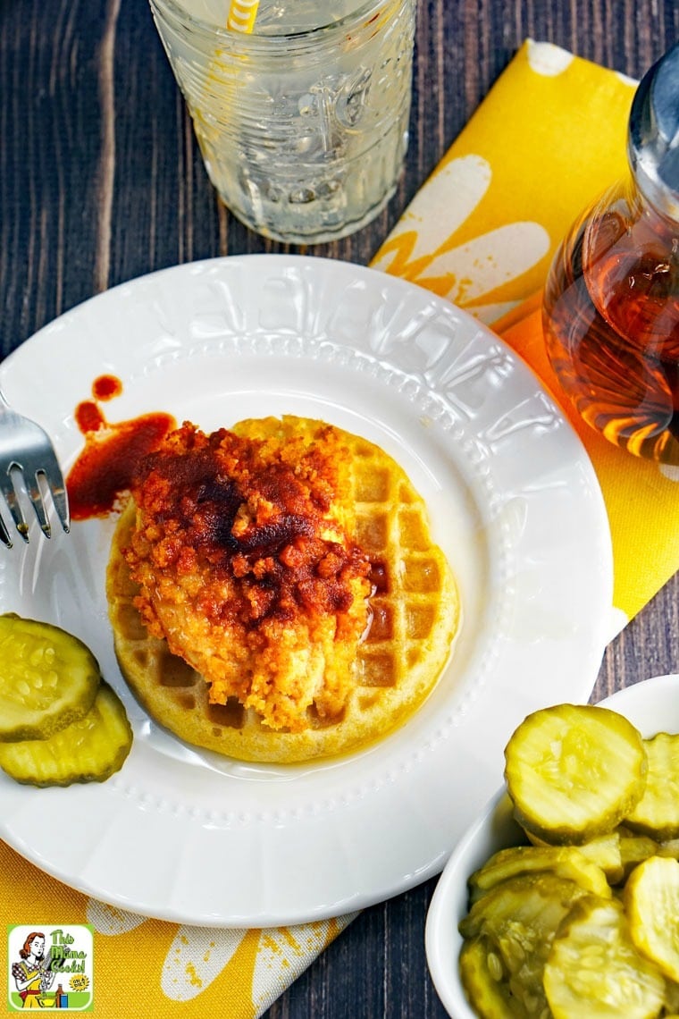 Overhead view of Chicken and Waffles, a glass of water, yellow napkin, syrup pitcher, and a plate of pickles.