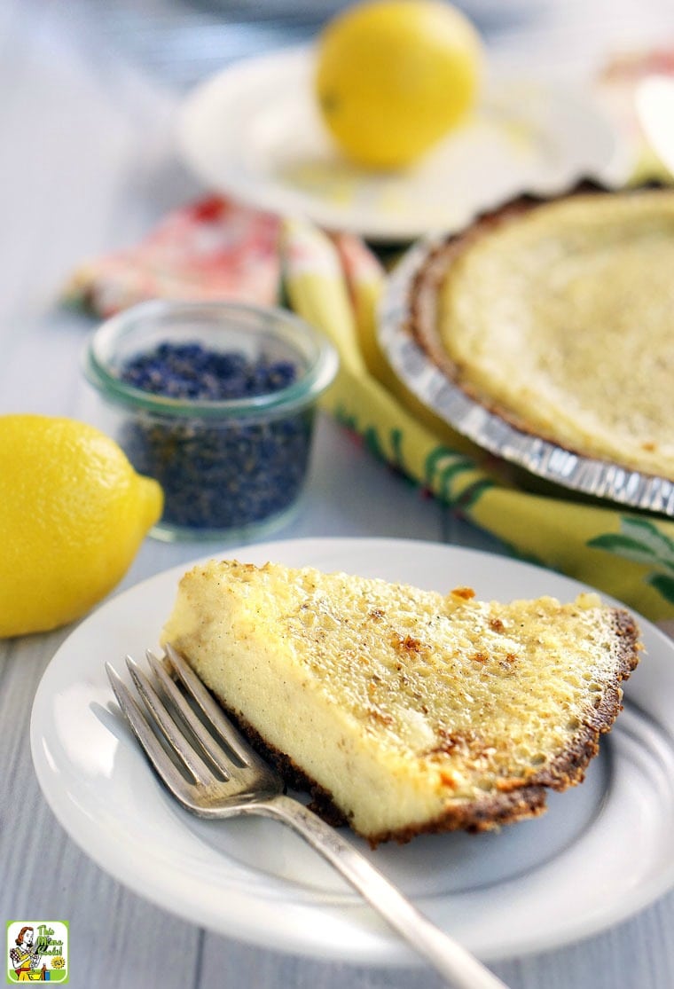 Closeup of a slice of homemade buttermilk pie on a white plate with a fork with a lemon and a jar of dried lavender.
