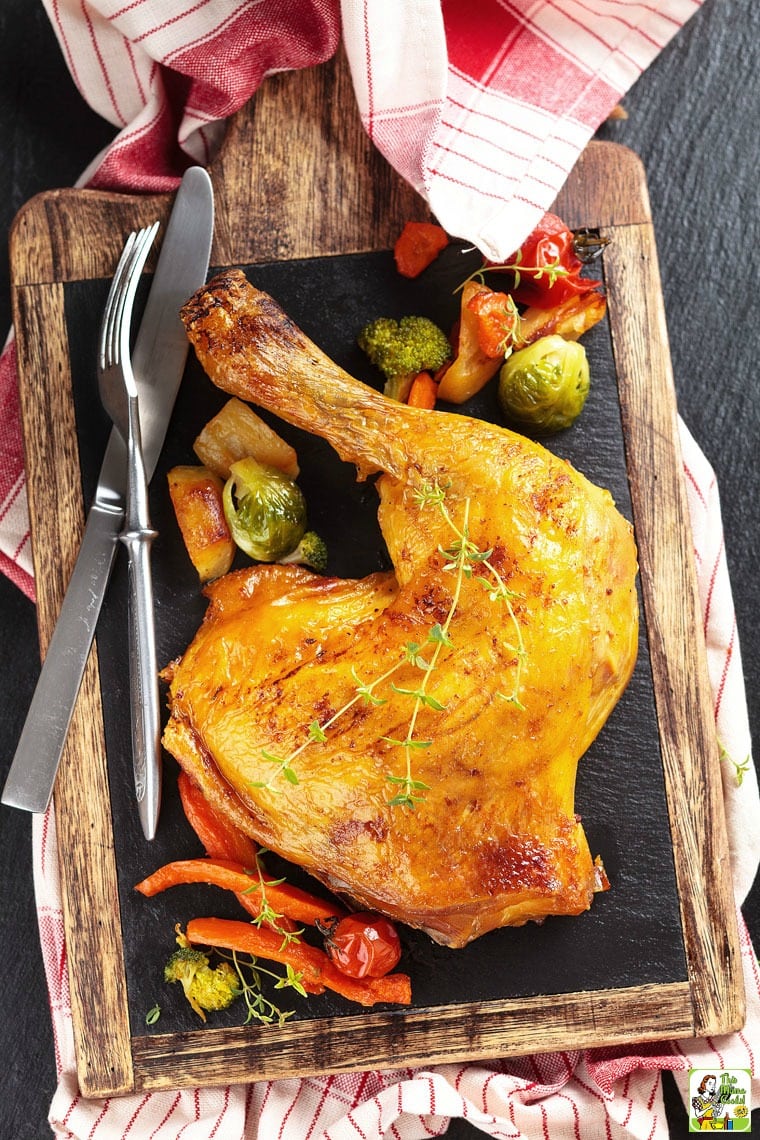 Smoked chicken quarters on a cutting board with a fork and knife with roasted vegetables.