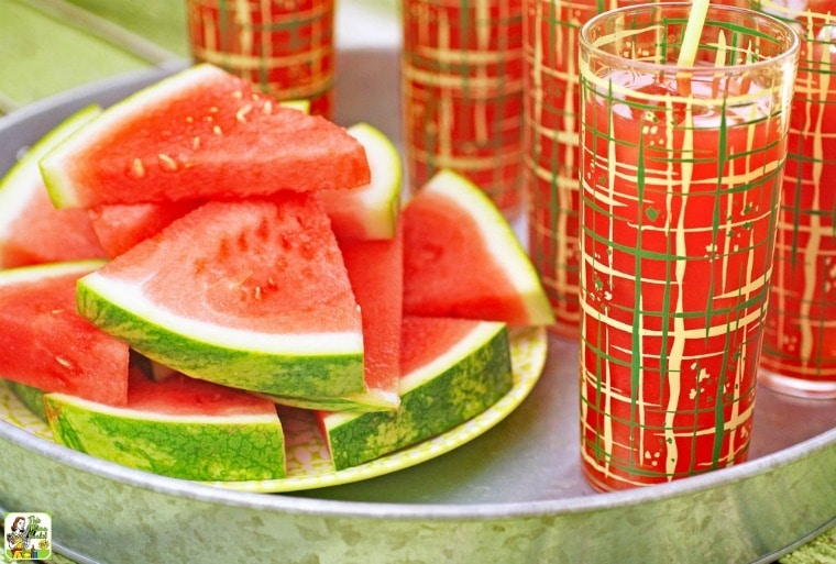 Glasses of Fruit Stand Watermelon Cocktails with a plate of watermelon slices on a metal tray.