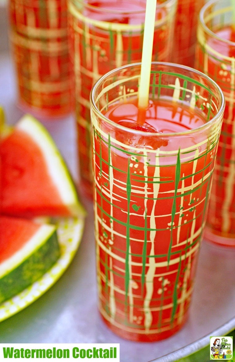 A glass of watermelon cocktail in a tall glass on a metal tray with slices of watermelon.