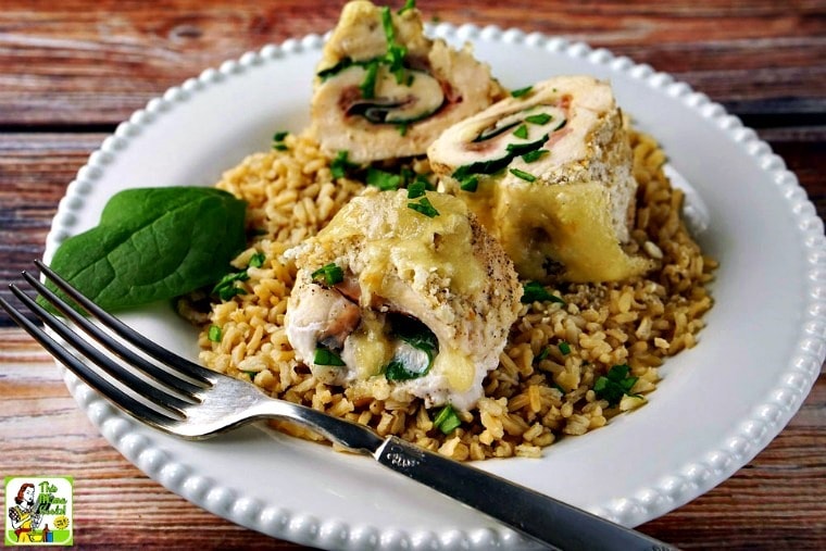 A white plate with three pieces of sliced chicken cordon bleu served on rice with a fork.