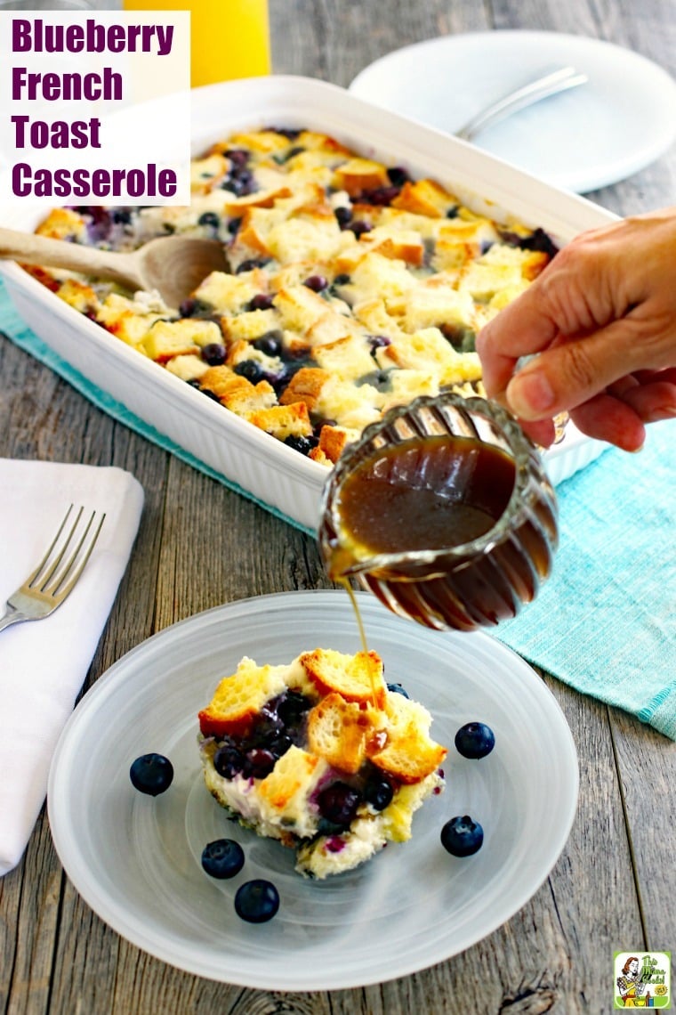 Blueberry French Toast Casserole in a white plate with maple syrup being poured from a small glass pitcher with a large platter of the casserole in the background.
