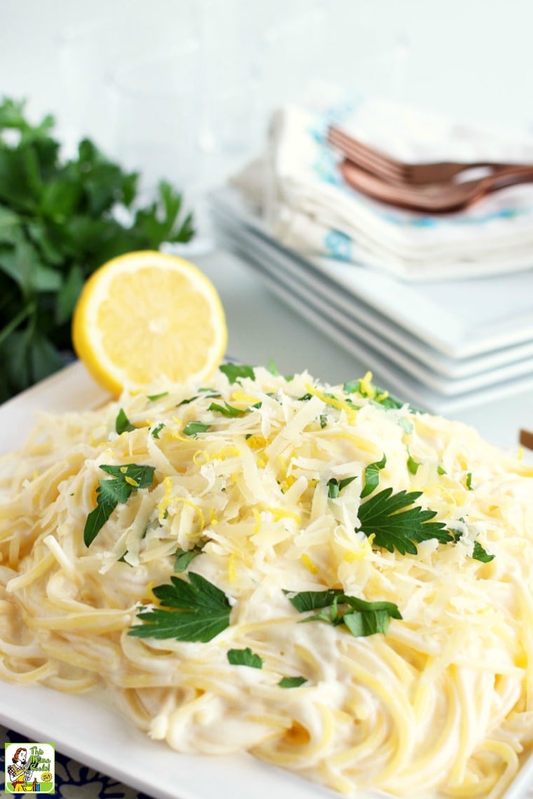 A dish of simple lemon pasta with parsley, half a lemon, and plates, naplins and forks in the background.
