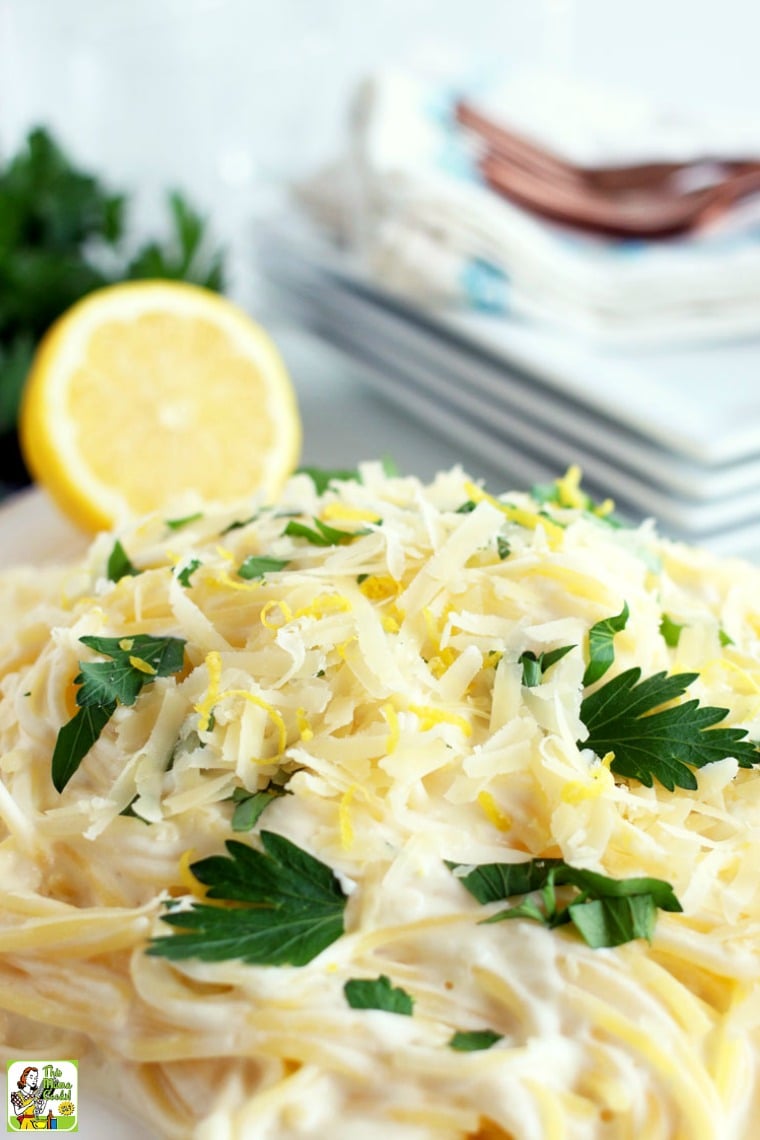 Closeup of lemon pasta recipe with a slice of lemon. Plates, napkins, and forks in the background.