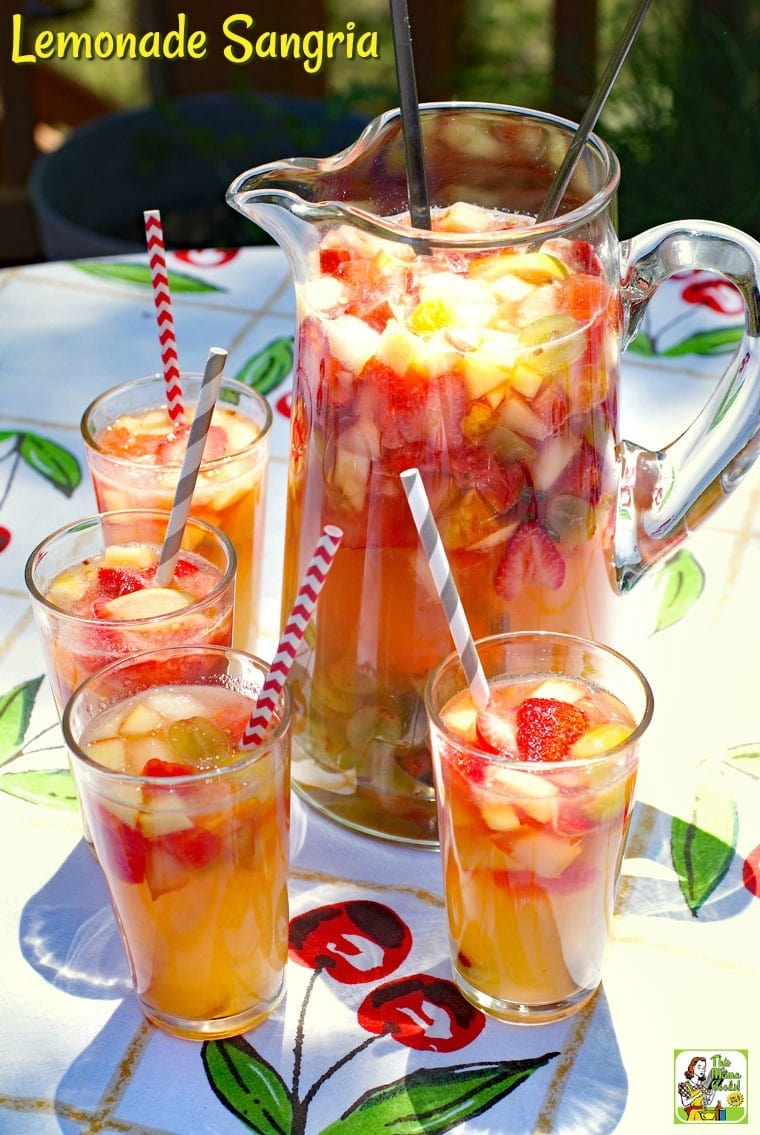 A pitcher and glasses of Lemonade Sangria on a colorful fruit patterned tablecloth.