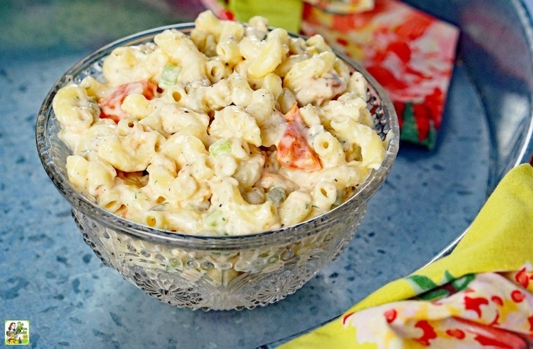 A glass bowl of Seafood Pasta Salad on a metal tray with floral napkins.