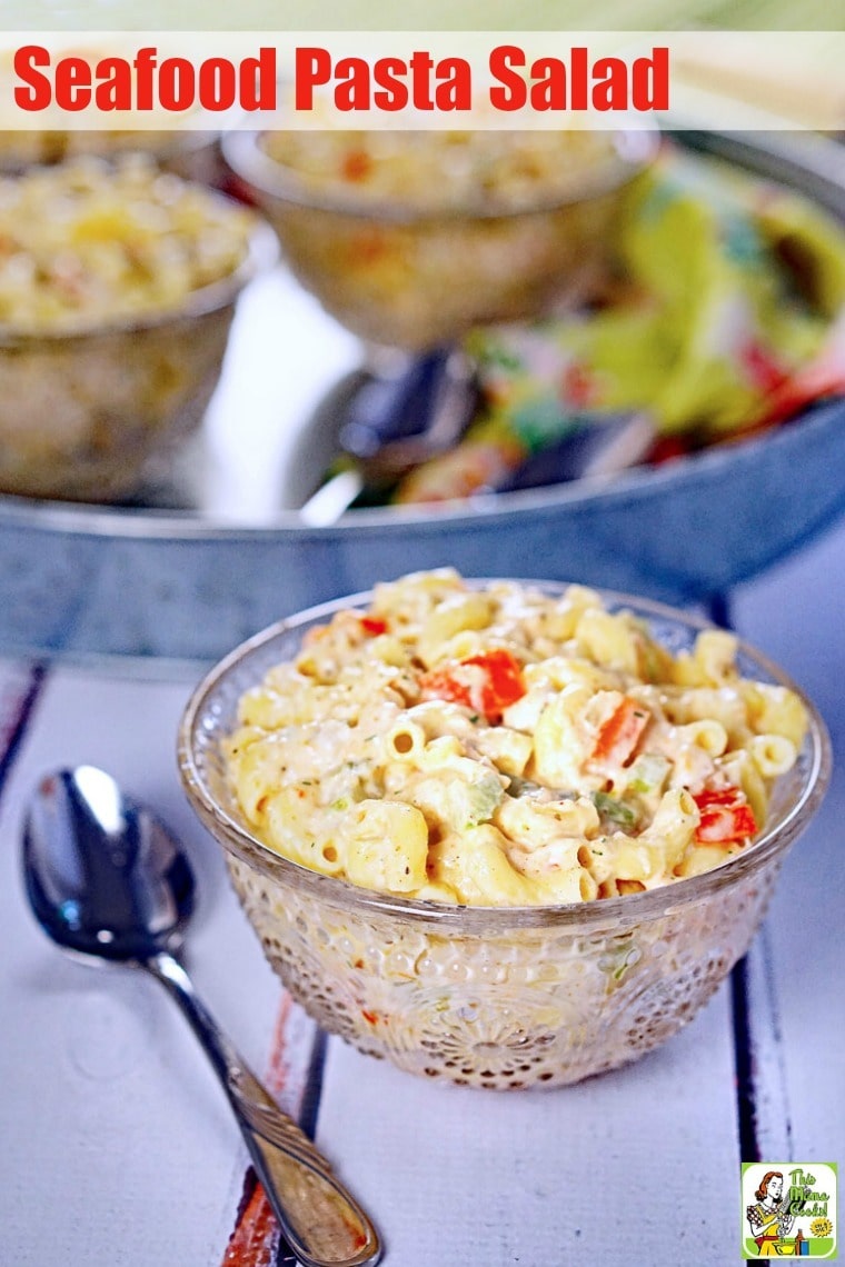 A glass bowl of Seafood Pasta Salad in front of a metal tray with spoon.