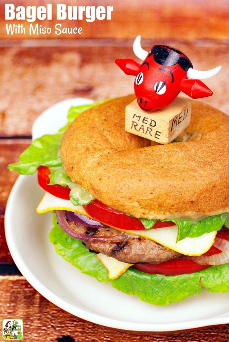 Bagel Burger with lettuce, onions, cheese, and tomatoes on a white plate.