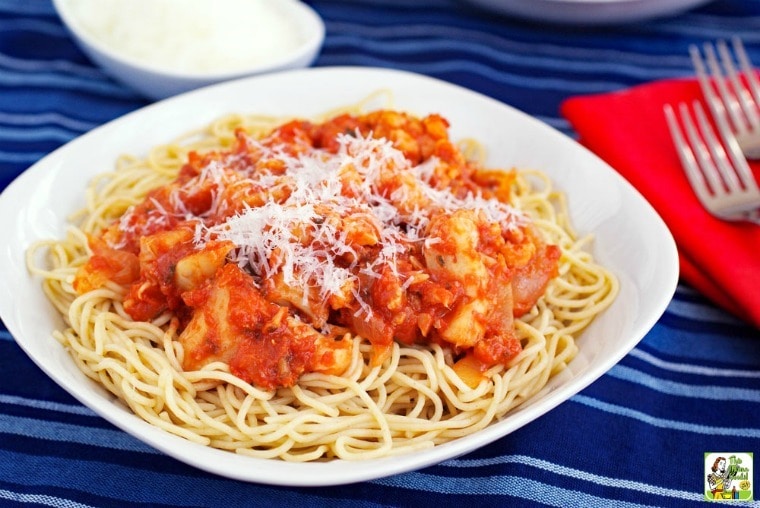A white bowl of Spicy Pasta with Cauliflower with red napkin and forks on a blue tablecloth.
