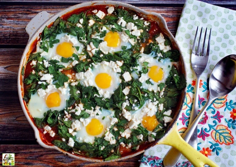Shakshuka with Feta in a yellow skillet with floral cloth napkin, serving spoon and fork.