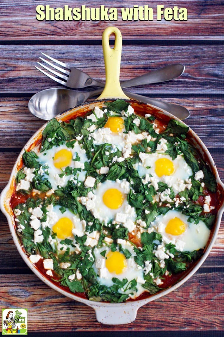 Overhead view of shakshuka with feta in a yellow skillet with silver serving spoon and fork.