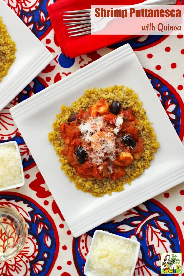 Bowls of shrimp puttanesca on quinoa on a red and blue tablecloth with a glass of wine, small bowls of shredded cheese, a red napkin, and forks.