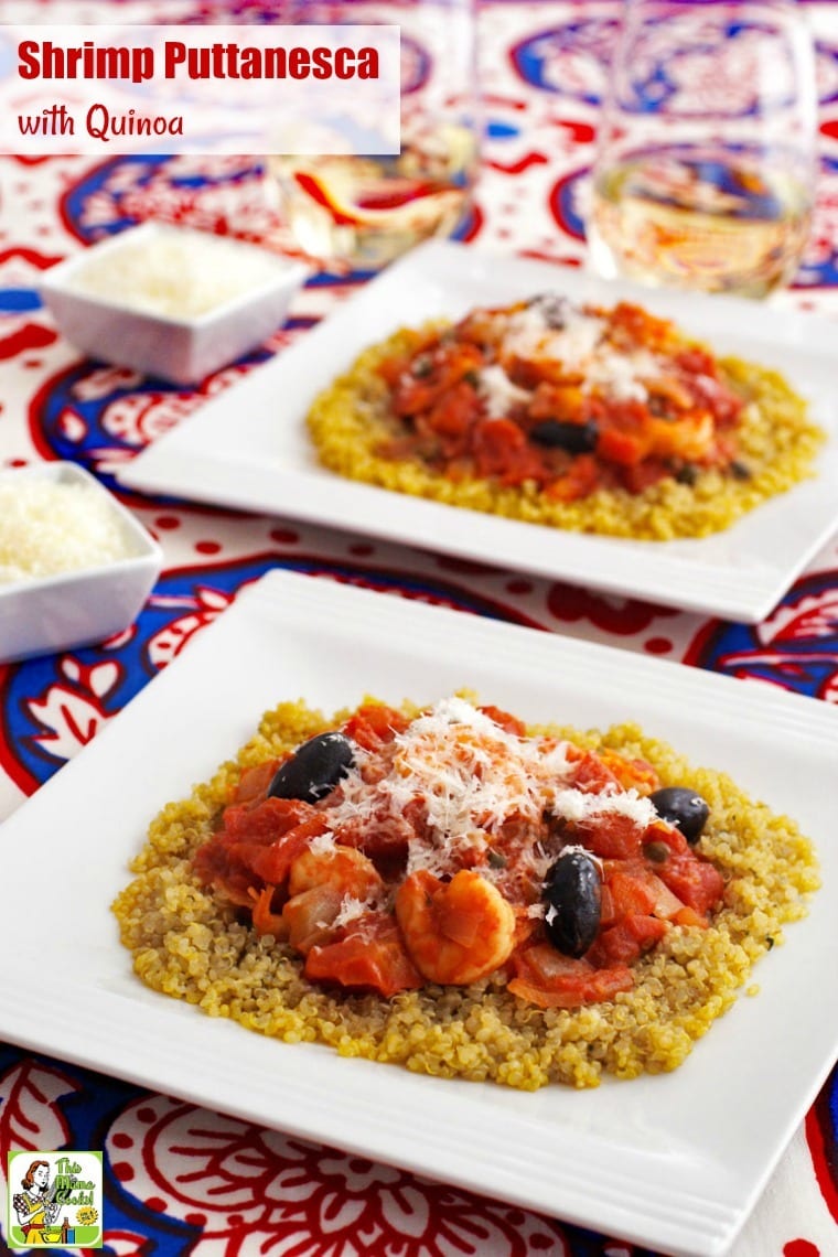 White dishes shrimp puttanesca with quinoa on a red, white and blue tablecloth, glasses of white wine, and small bowls of shredded cheese.