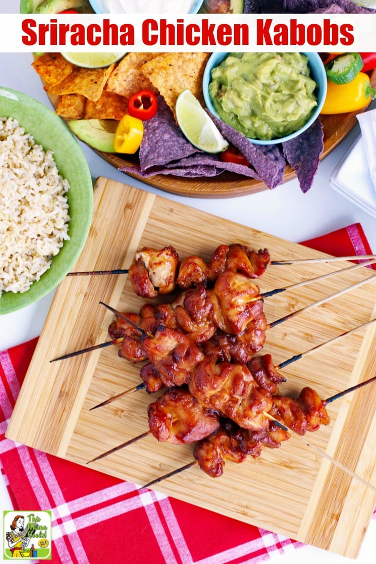Skewers of Chicken Kabobs on a wooden platter with a bowl of rice, and bowl of guacamole and tortilla chips.