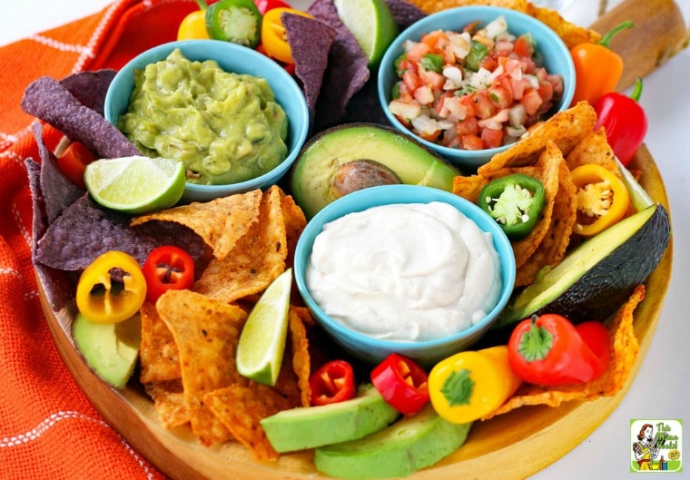 Overhead view of a platter with a bowls of sour cream, salsa, and guacamole with dippers of sweet peppers and tortilla chips.