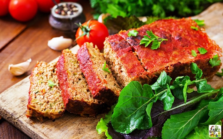 Smoked Meatloaf on a wooden cutting board with herbs, tomatoes, garlic, and seasonings.