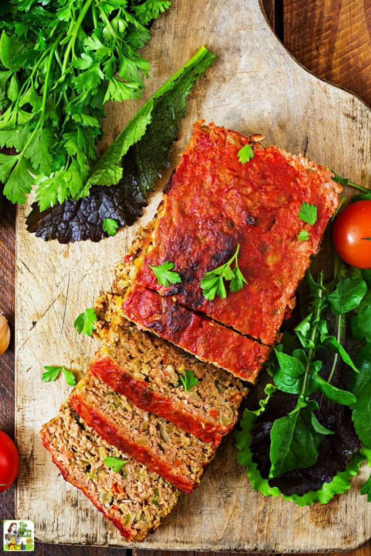 Overhead shot of sliced meatloaf on a wooden cutting board with lettuce and tomatoes.