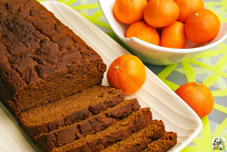 A loaf of Gluten Free Pumpkin Bread on a platter with a bowl of tangarines on a green placemat.