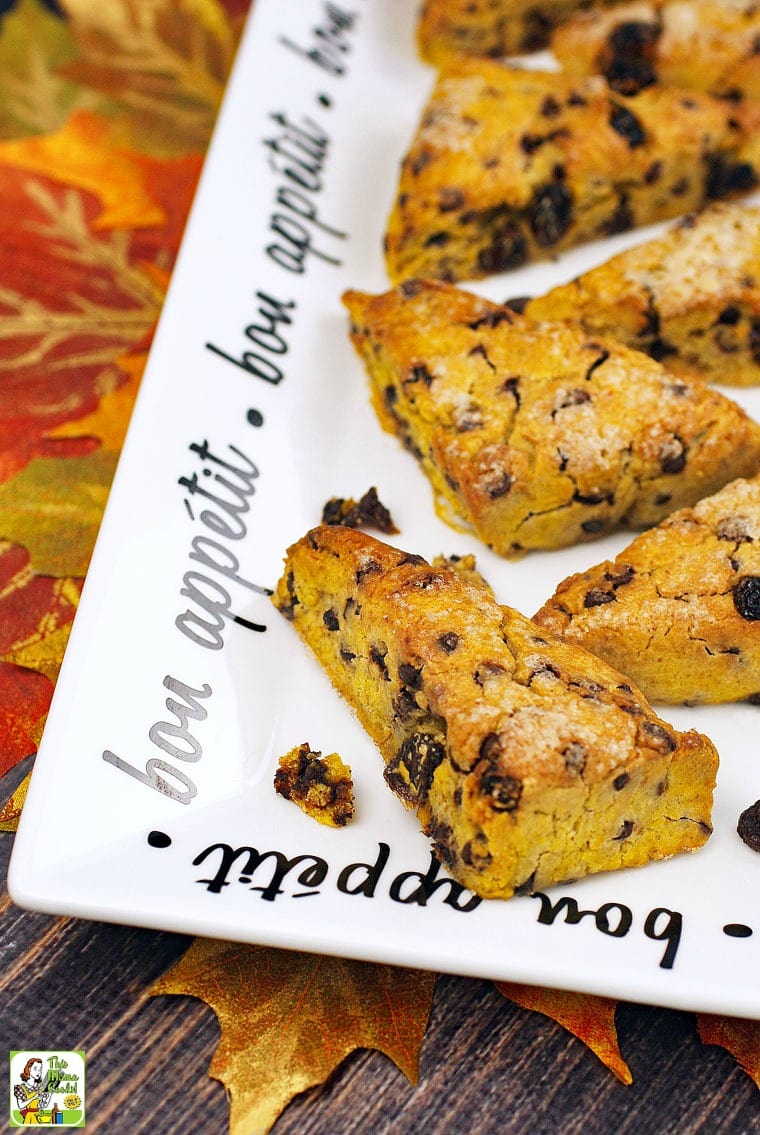 A platter of pumpkin scones with raisins and chocolate chips on a table of fall leaves.