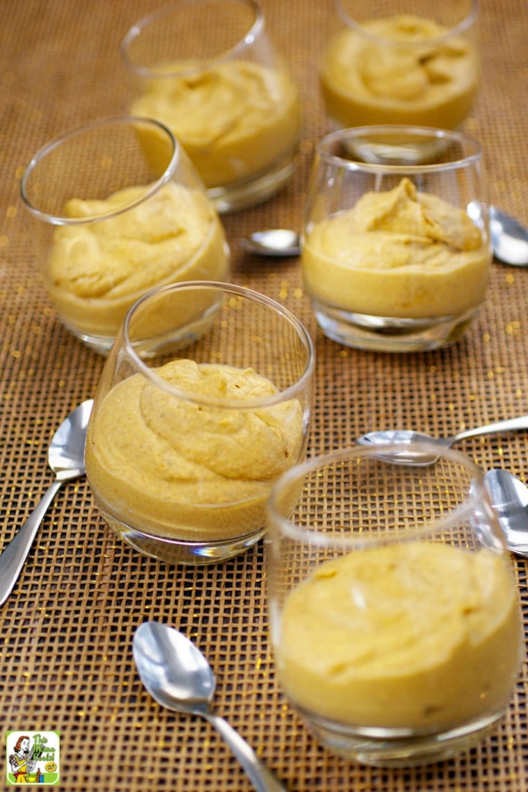 A tabletop of many glasses of pumpkin pie mousse with small spoons.