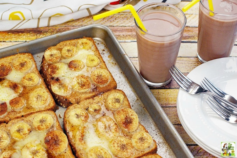 Oven Baked French Toast Recipe with Pumpkin & Bananas on a baking sheet with glasses of chocolate milk, plates and forks.