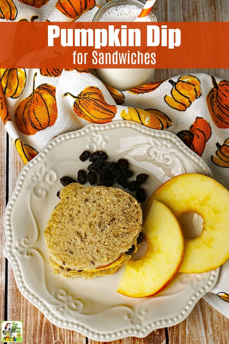 Pumpkin dip sandwich on a plate with raisins and slices of apple on a pumpkin print tea towel with a glass of milk.