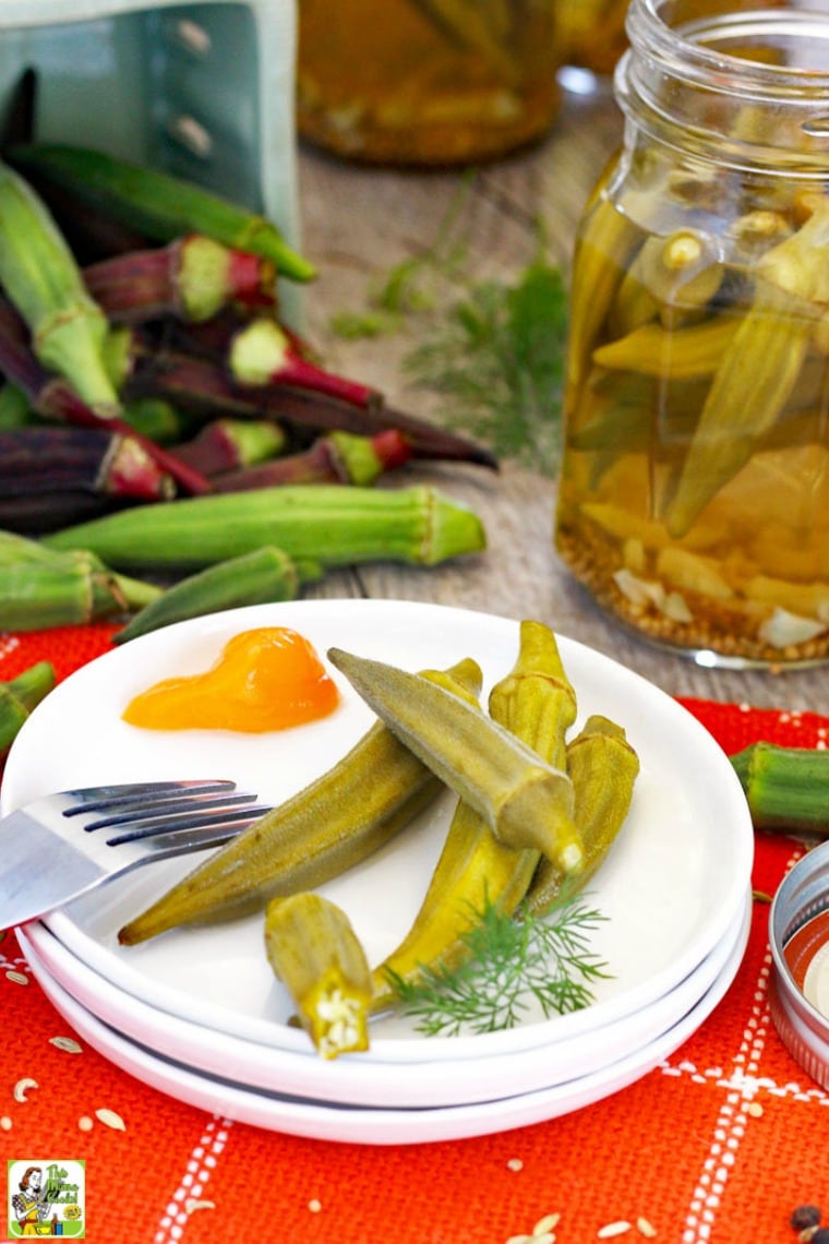 A plate of pickled okra with jars of pickled okra and raw okra in the background.