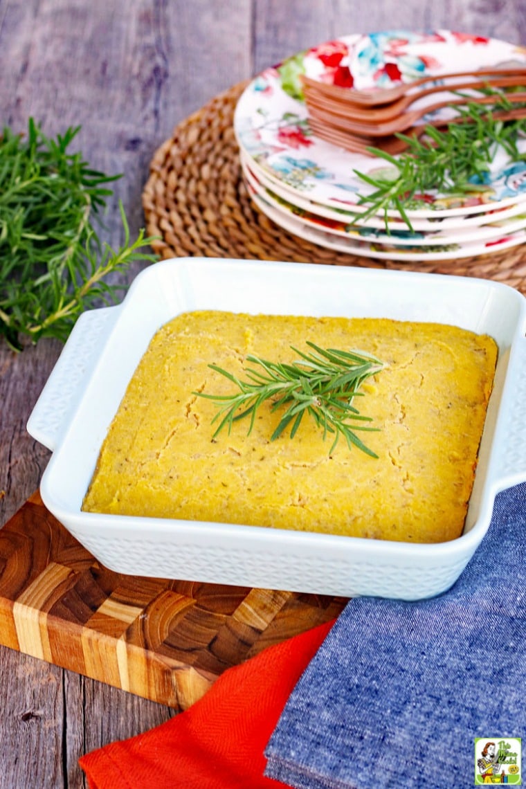 A baking dish of vegan cornbread with a sprig of rosemary and plates and forks in the background.