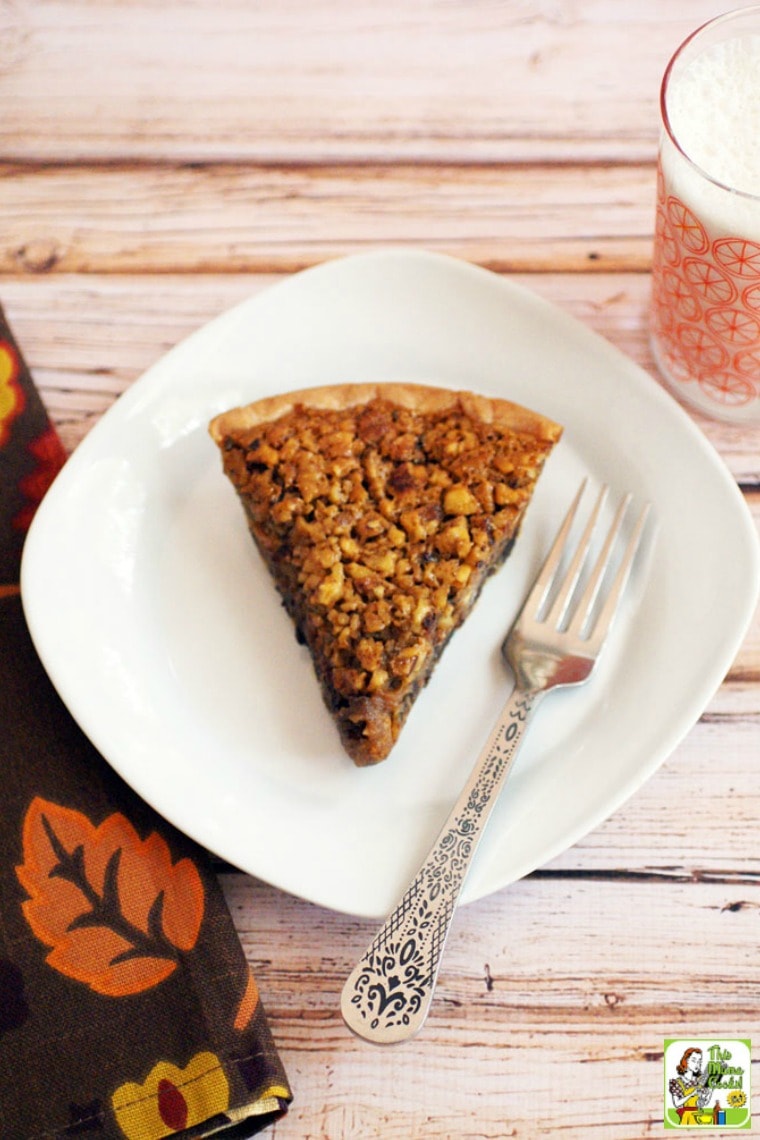 Overhead shot of slice of pecan pie on white plate with silver fork and a glass of milk in vintage glass.