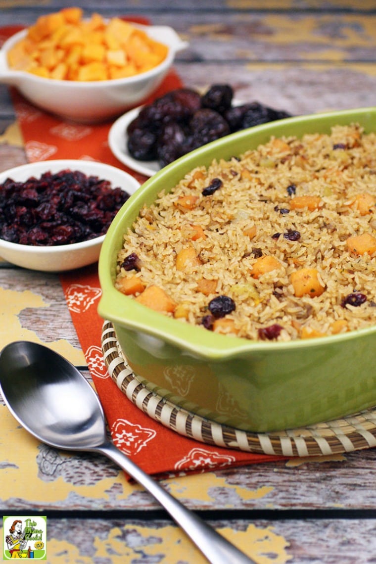 A casserole dish of rice stuffing with bowls of cranberries, squash and dates and a silver serving spoon.