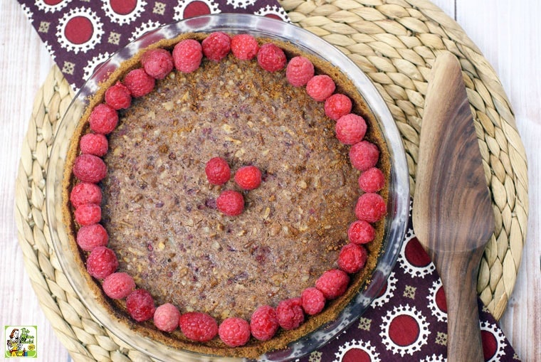 Overhead view of a gluten free pecan pie with raspberries on a woven mat with a napkin and wooden pie server.