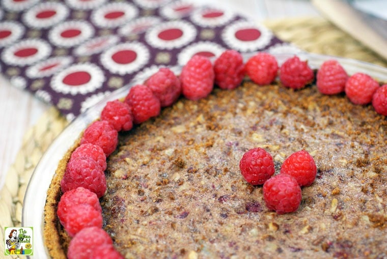 Overhead shot of gluten free pecan pie with raspberries on a woven mat with napkin.