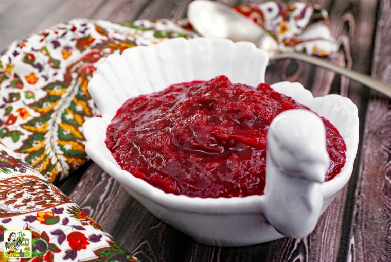 A white turkey shaped bowl of Cranberry Sauce, a colorful napkin, and a silver serving spoon.