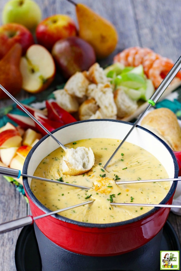 Fondue forks dipping bread into brie fondue pot. Cheese fondue dippers in background.