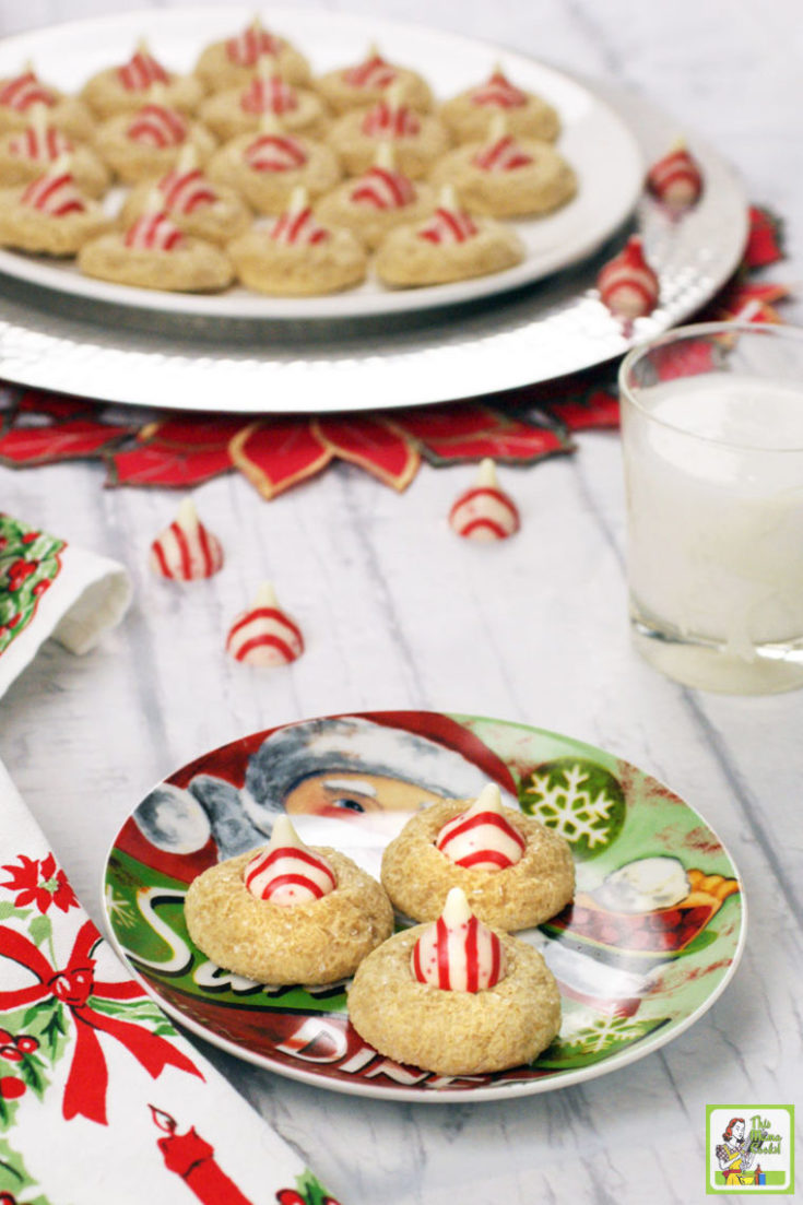 Two holiday plates of Peppermint Thumbprint Hershey Kiss Cookies with a glass of milk.