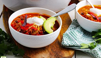 White bowls of 7 Can Taco Soup with dollops of sour cream and a slice of avocado on a wooden cutting board and a green and white napkin.