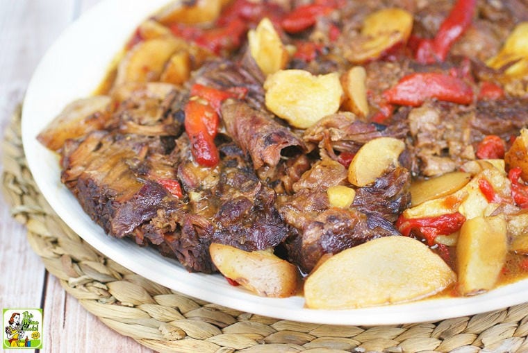 A bowl of Crock Pot Mississippi Pot Roast with red peppers and potato wedges on a woven straw mat.
