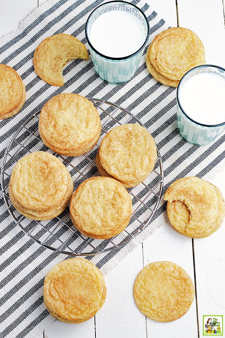 Overhead shot of rice flour snickerdoodles cookies on a striped napkin and wire rack with glasses of milk.