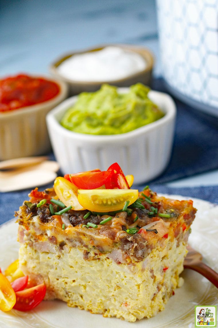 A serving of breakfast casserole with hashbrowns and vegetables on a plate served with sour cream, salsa and guacamole.