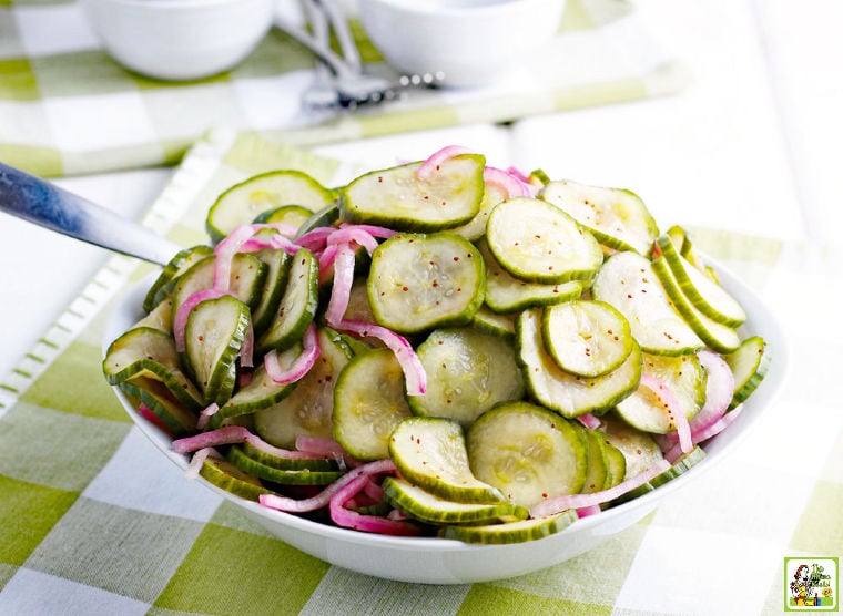 A bowl of Cucumber Onion Salad on a checkered napkin with serving spoon.