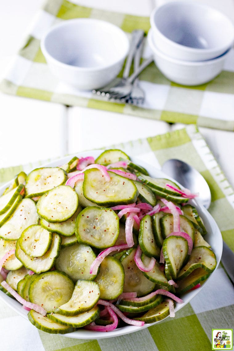 A bowl of Cucumber Onion Salad with white bowls, forks and green napkins in the background.