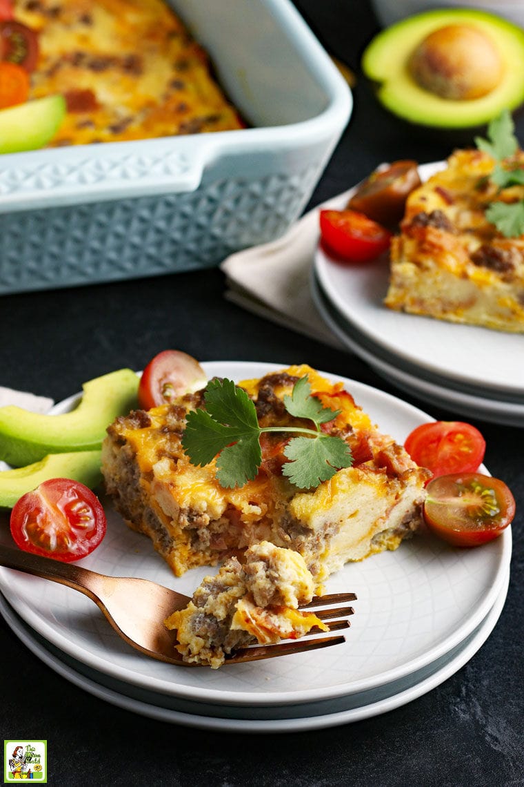 A white plate of a breakfast casserole with avocados and tomatoes.