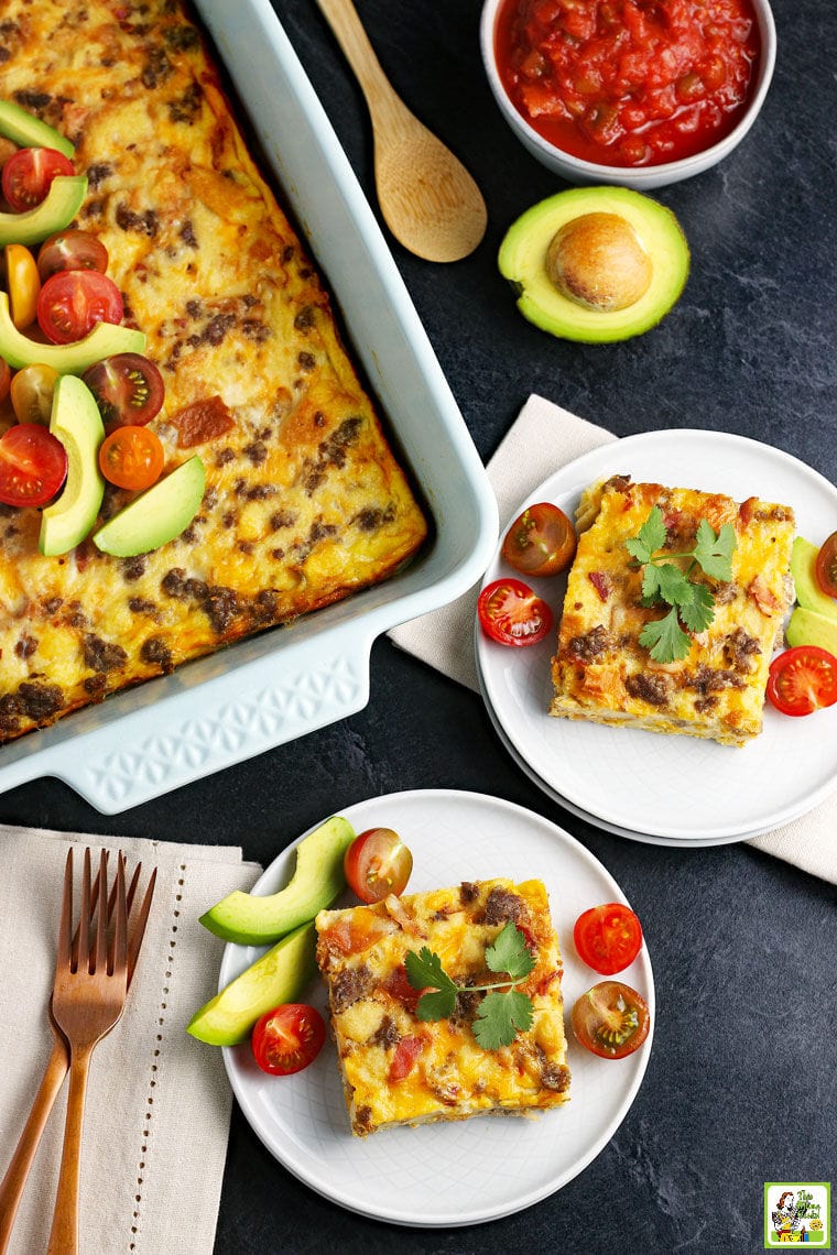 White plates a cheesy breakfast casserole with a large baking dish. Served with tomatoes and avocados.