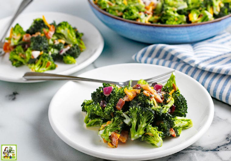 A large bowl and two white plates of Broccoli Bacon Salad with striped napkin.